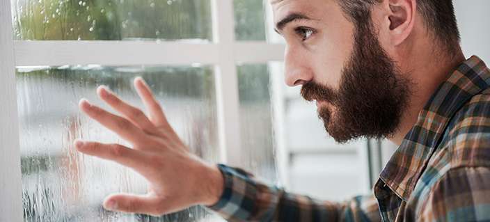 Rainy mood. Thoughtful young bearded man touching the window and